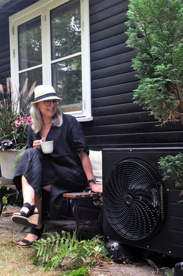 Lene Nissen sidder ved siden af varmepumpen, som hun har malet sort
