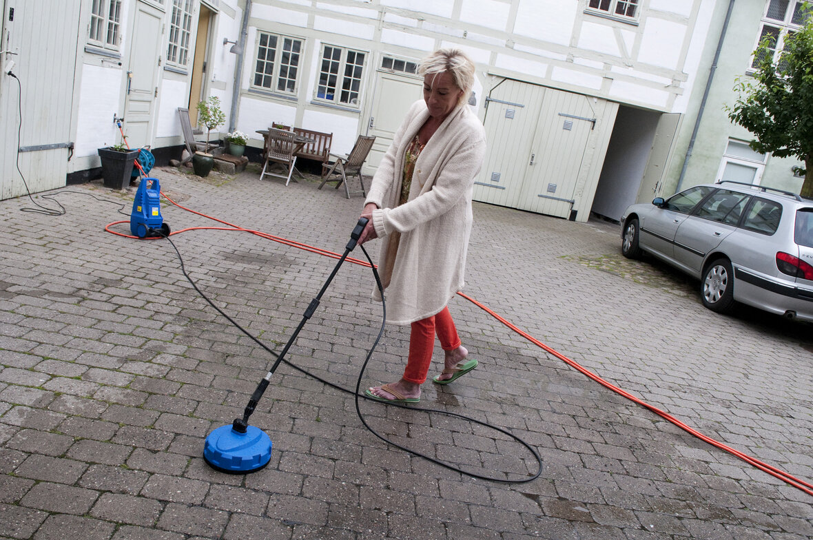 Person bruger rengøringsmaskine på flisebelagt gårdsplads.